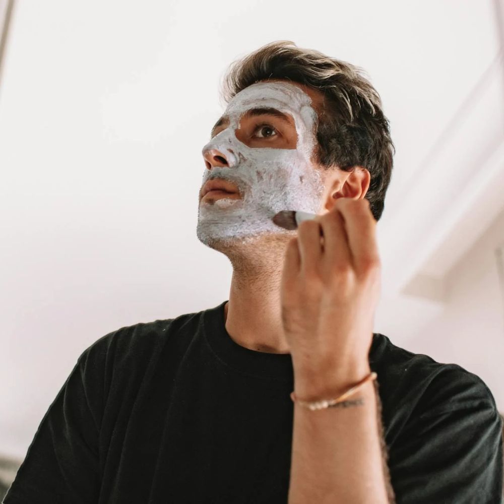 Man applying a face mask to his face with a neutral background